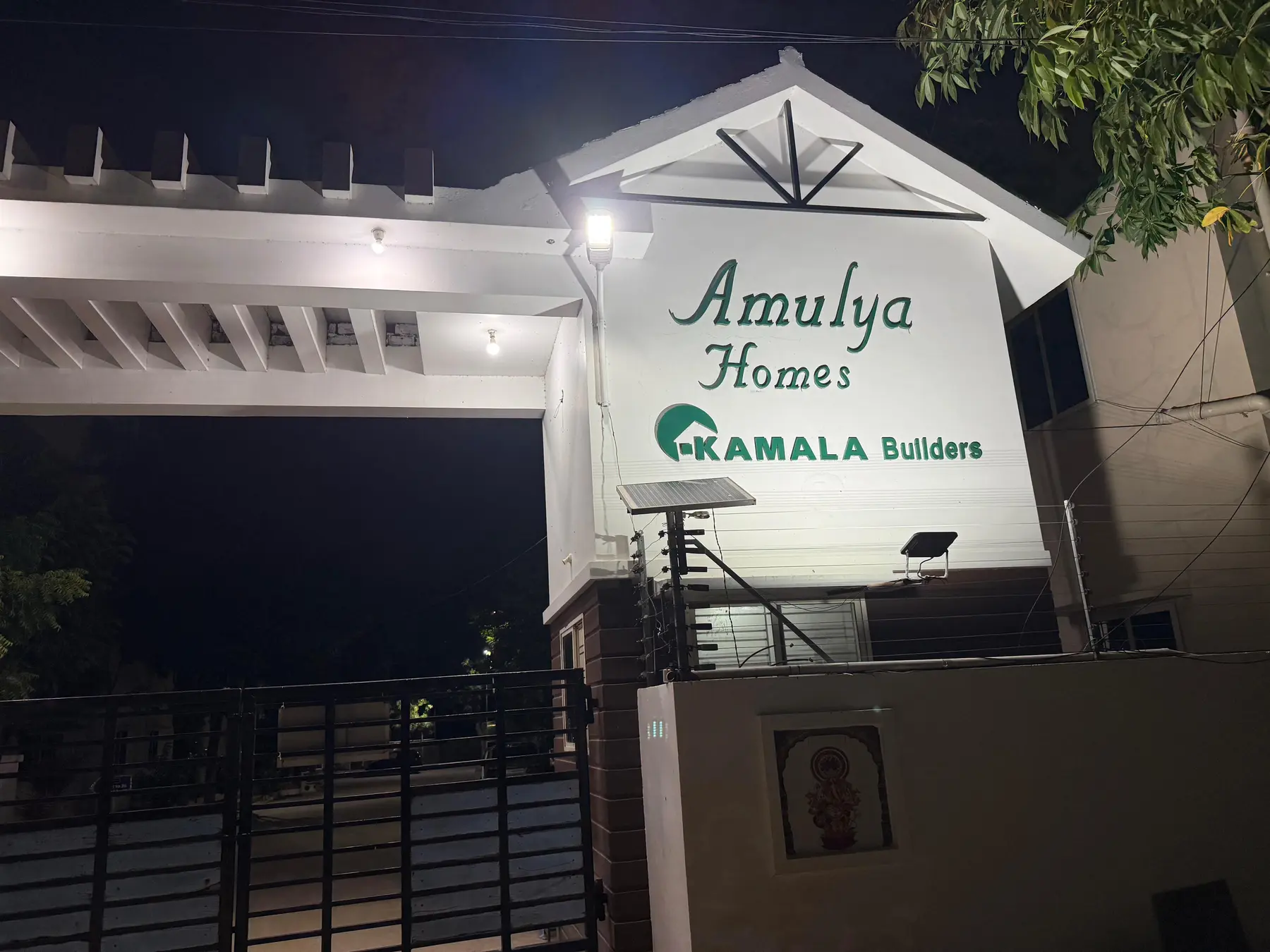 The lit Amulya Homes sign at the main gate at night